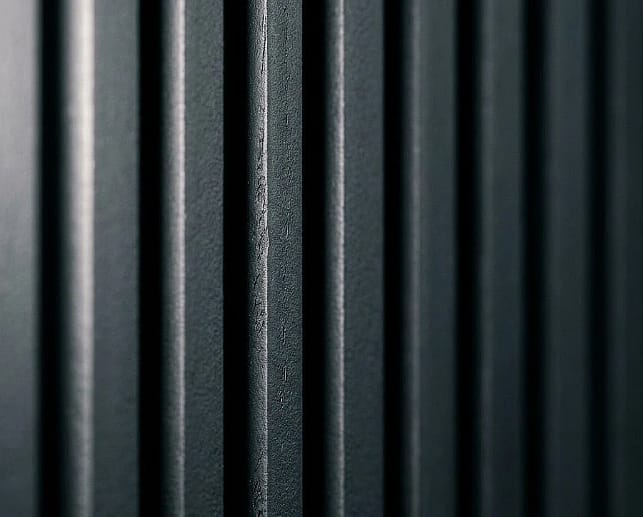 A detailed close-up view of parallel dark charcoal grey fluted wood panels, showing a detailed textured matte finish and deep vertical shadow lines.