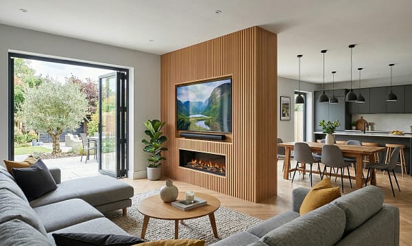 Bespoke peninsula media wall projecting into a modern UK kitchen-diner with TV and soundbar on one face and oak slat panels on the reverse.