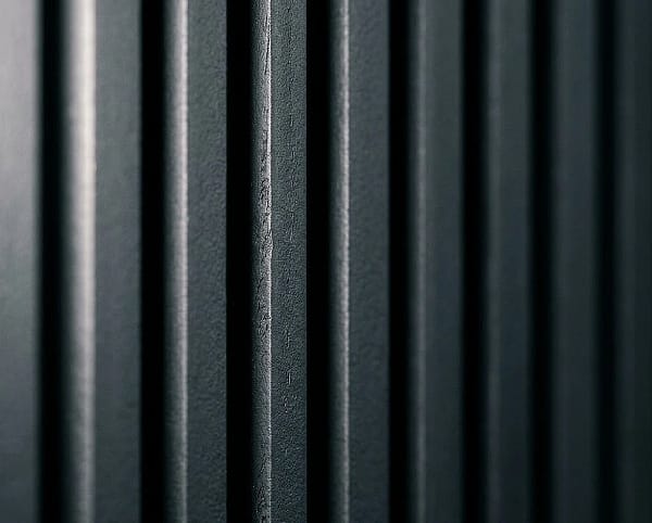A detailed close-up view of parallel dark charcoal grey fluted wood panels, showing a detailed textured matte finish and deep vertical shadow lines.